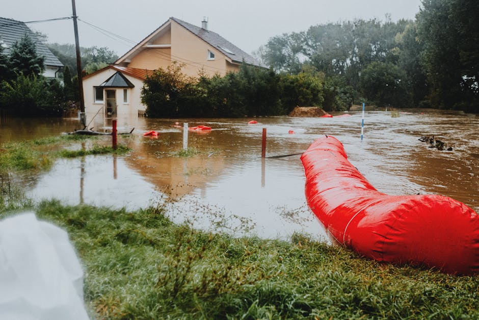 Image depicting a residential street in Woking station area during a flood, with several emergency responders in high-visibility and protective clothing working together to manage floodwaters and sand